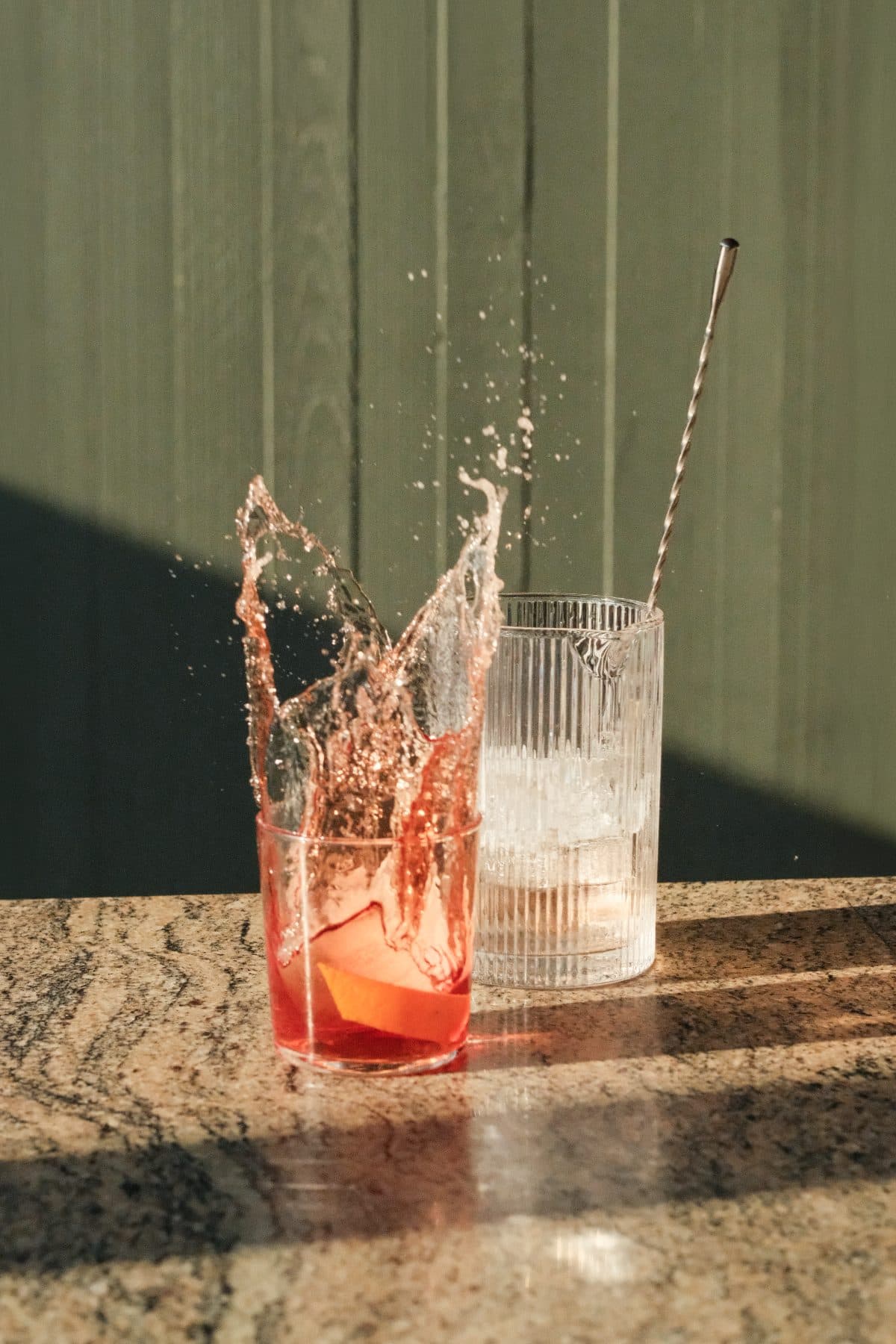 A cocktail mid-splash on the bar, afternoon sun across the counter